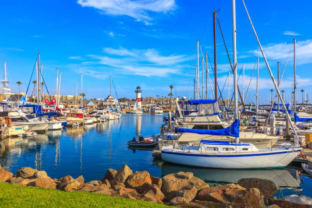 Rows of small boats and yachts are aligned in the San Diego marina, with a lighthouse in the back.